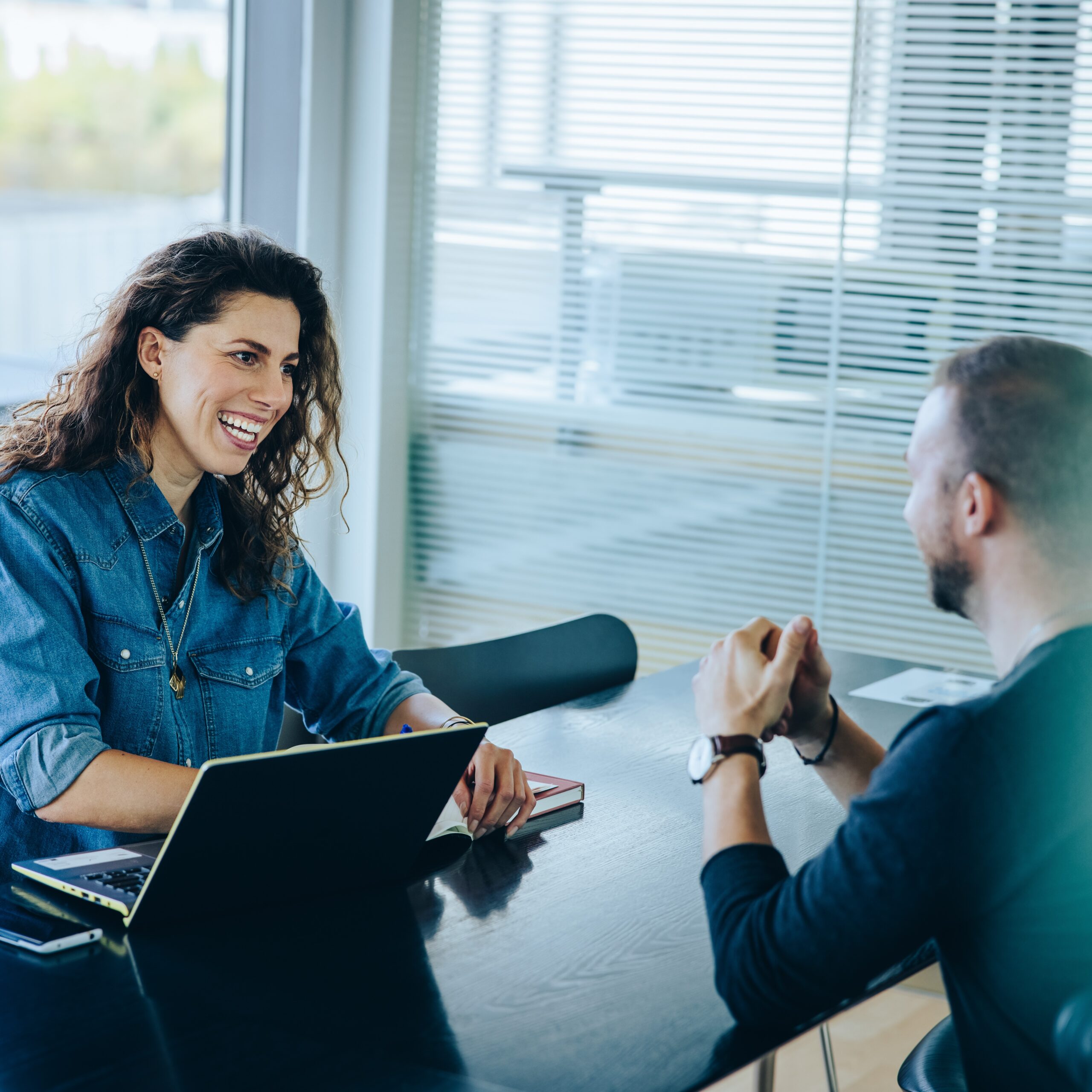 A man and a woman sitting across from one another at a black table talking to one another